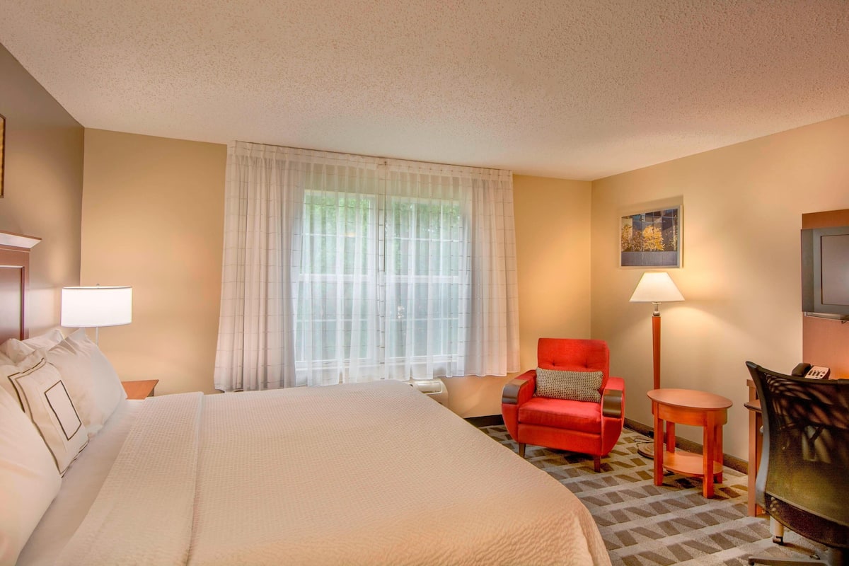 A hotel room with a large bed, a red armchair, a small table, and a desk with a phone.