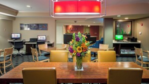 Une salle de conférence d’hôtel avec une table en bois, des chaises, un vase de fleurs, un comptoir d’accueil et un écran de télévision.