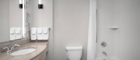 A bathroom with a granite countertop sink, a toilet, a bathtub, and a shower curtain.