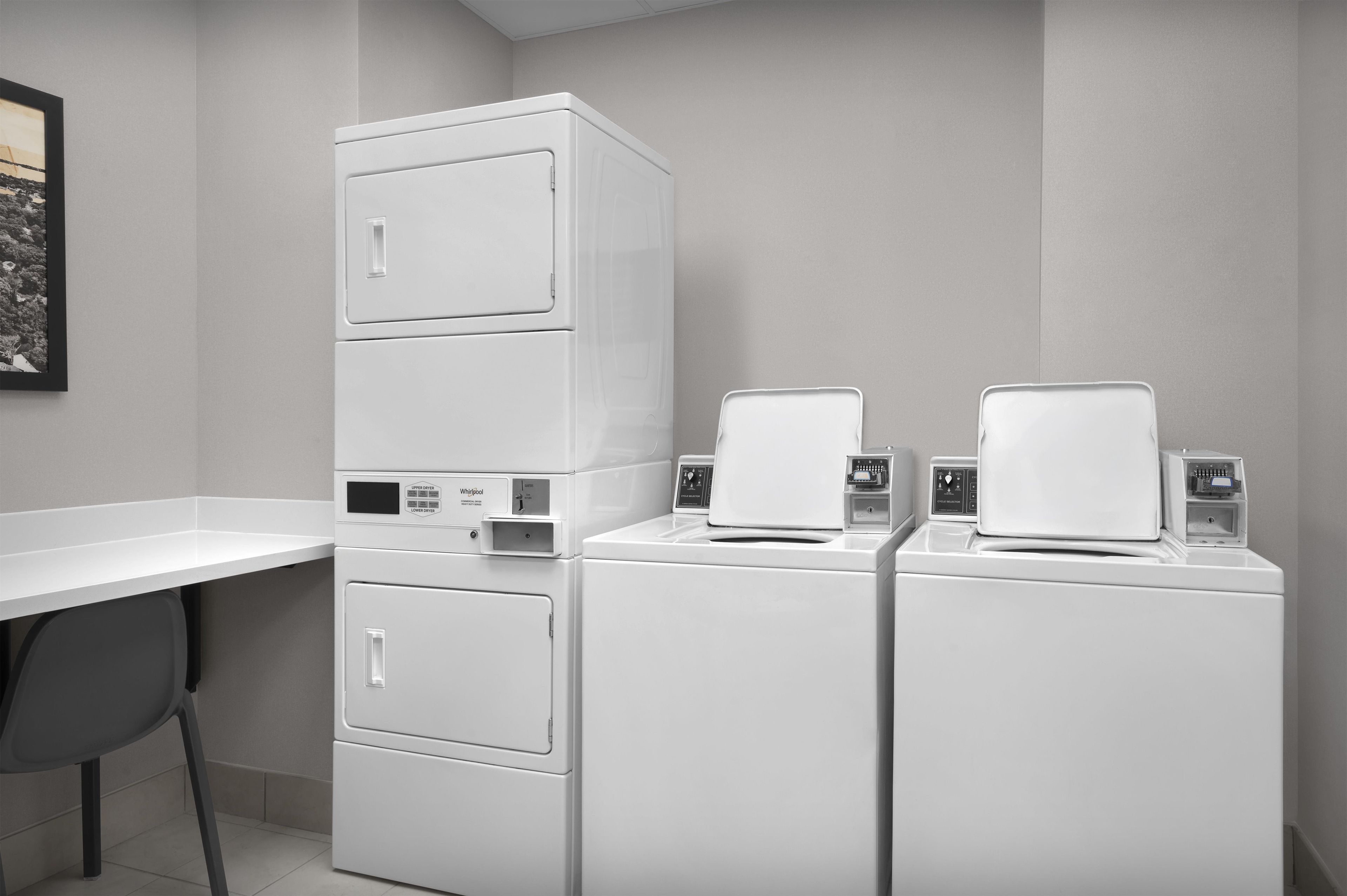A laundry area with stacked washers and dryers, a white countertop, and a chair.