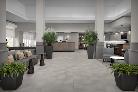 A modern lobby with a reception desk, seating area, and potted plants.