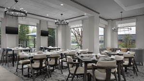 A hotel dining area with multiple tables and chairs, large windows, and a chandelier. - Hilton Garden Inn Annapolis (Annapolis)