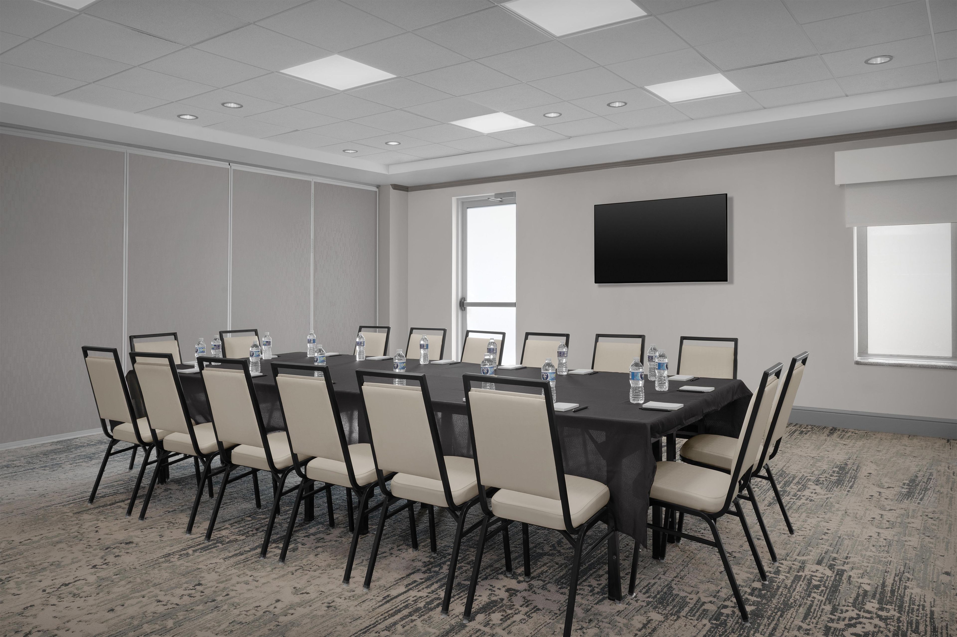 A conference room with a large table, chairs, water bottles, and a flat-screen TV on the wall.