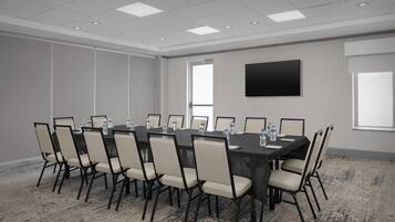 A conference room with a large table, chairs, water bottles, and a flat-screen TV on the wall.