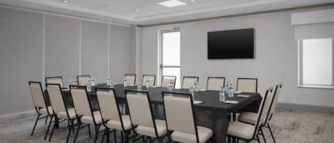 A conference room with a large table, chairs, water bottles, and a flat-screen TV on the wall.