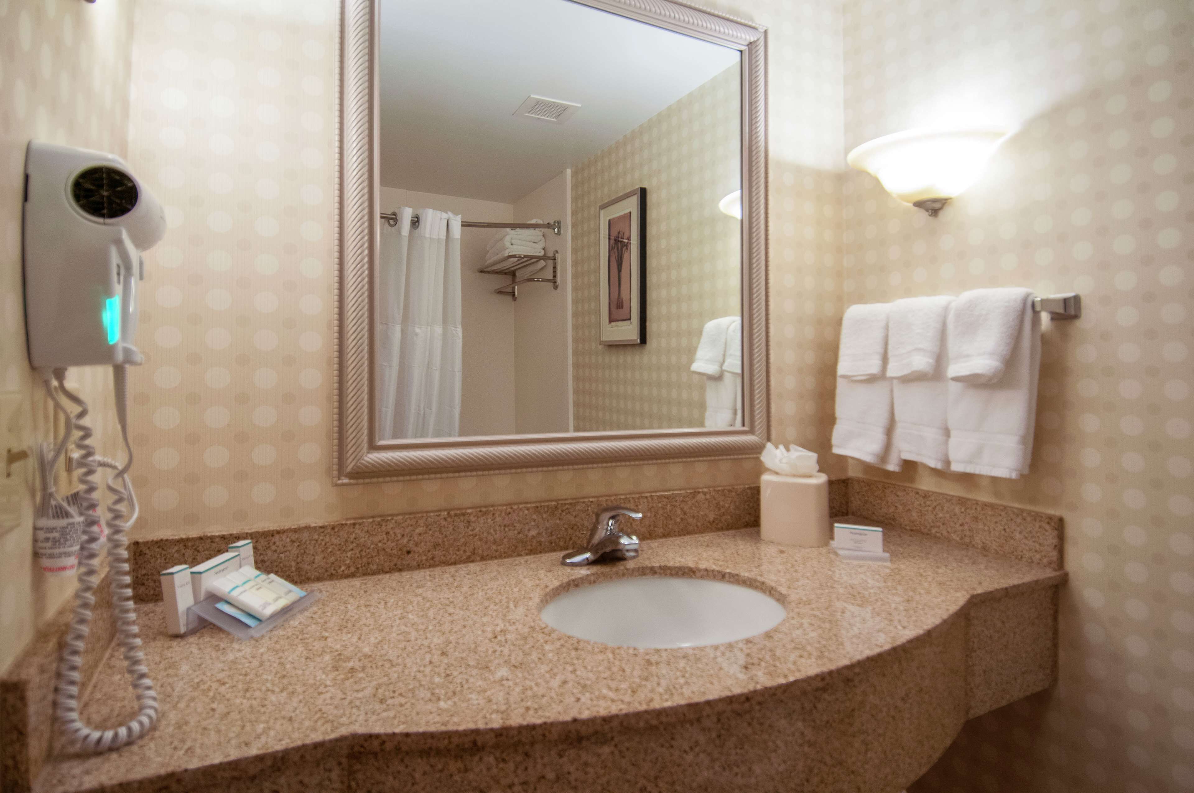 Un baño con lavamanos, espejo, secador de pelo y toallas en un perchero.