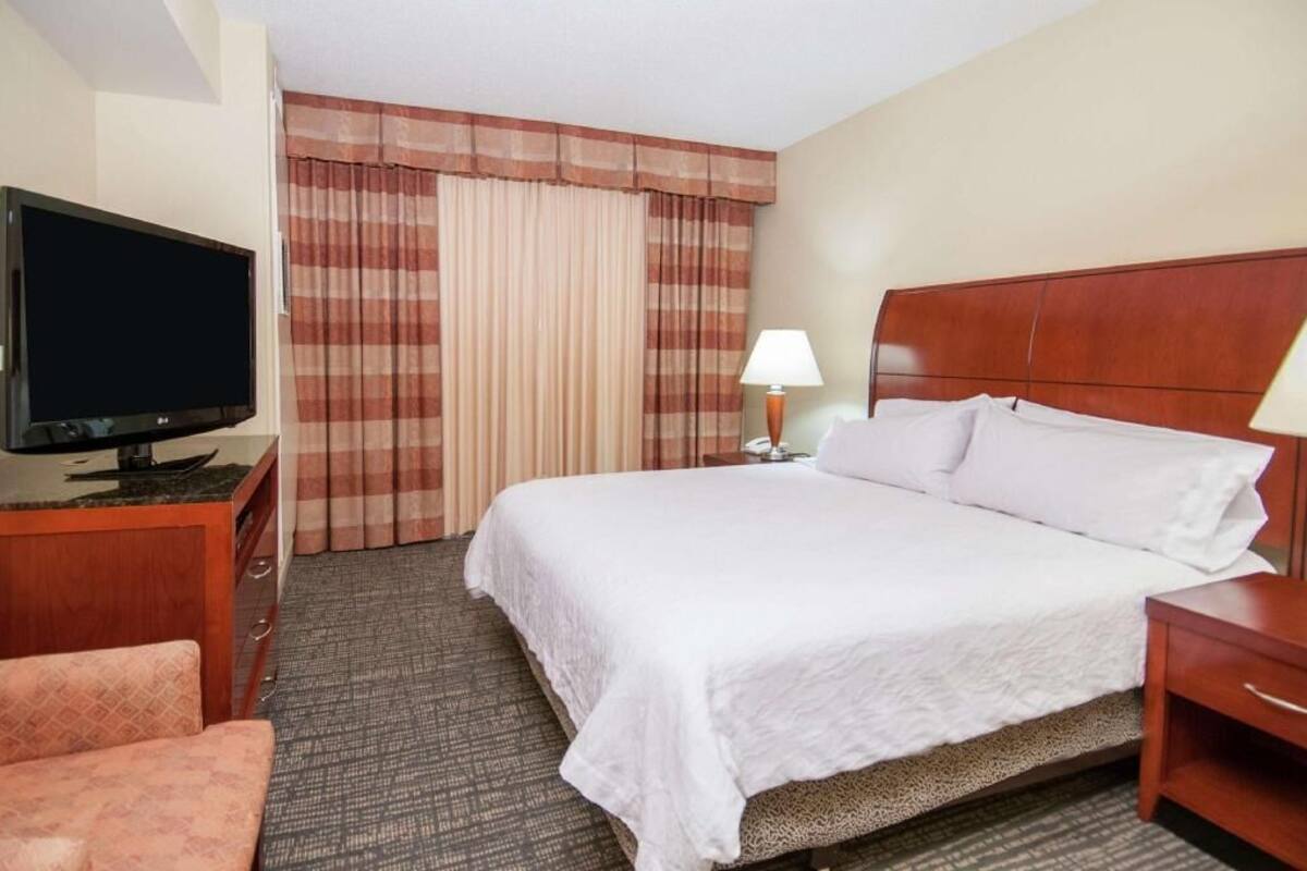 A hotel room with a bed, a television, a desk, a chair, a lamp, and curtains.
