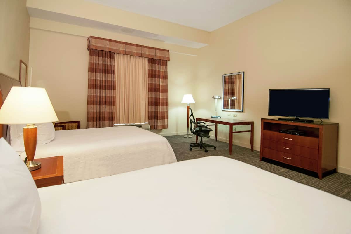 A hotel room with two beds, a desk with a chair, a television, and a lamp.