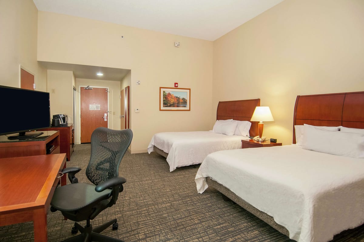 A hotel room with two beds, a desk with a chair, a television, and a painting on the wall.