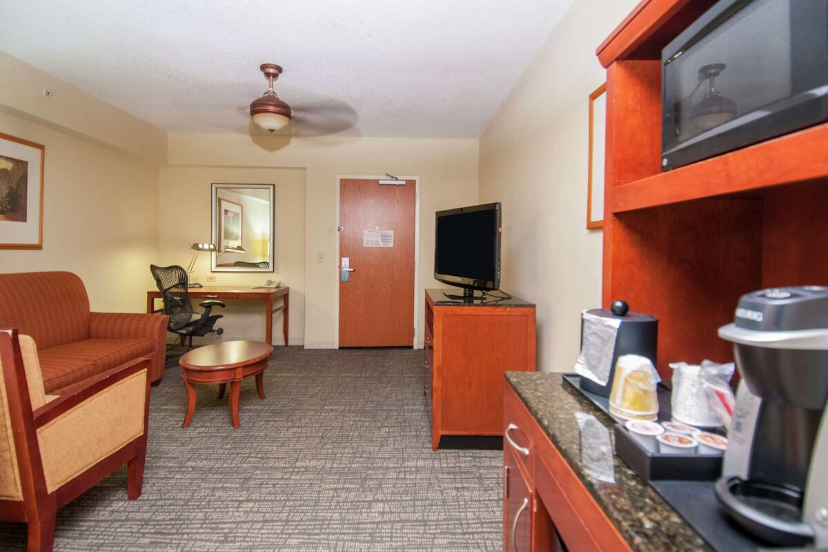 A hotel room with a sofa, a small table, a desk with a chair, a television, a coffee maker, and a microwave.