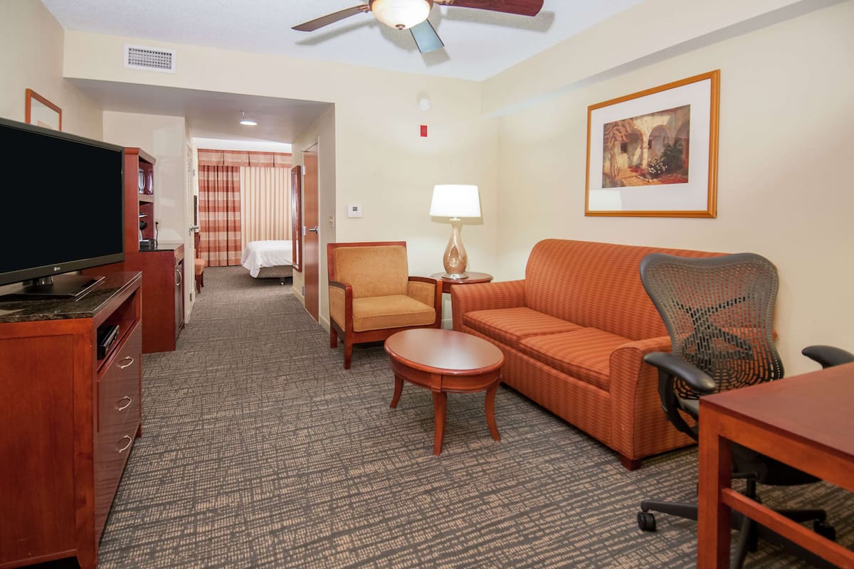 A hotel room with a television, a sofa, a chair, a small table, and a ceiling fan.