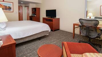 A hotel room with a bed, a desk with a chair, a television, a small round table, and a wardrobe.
