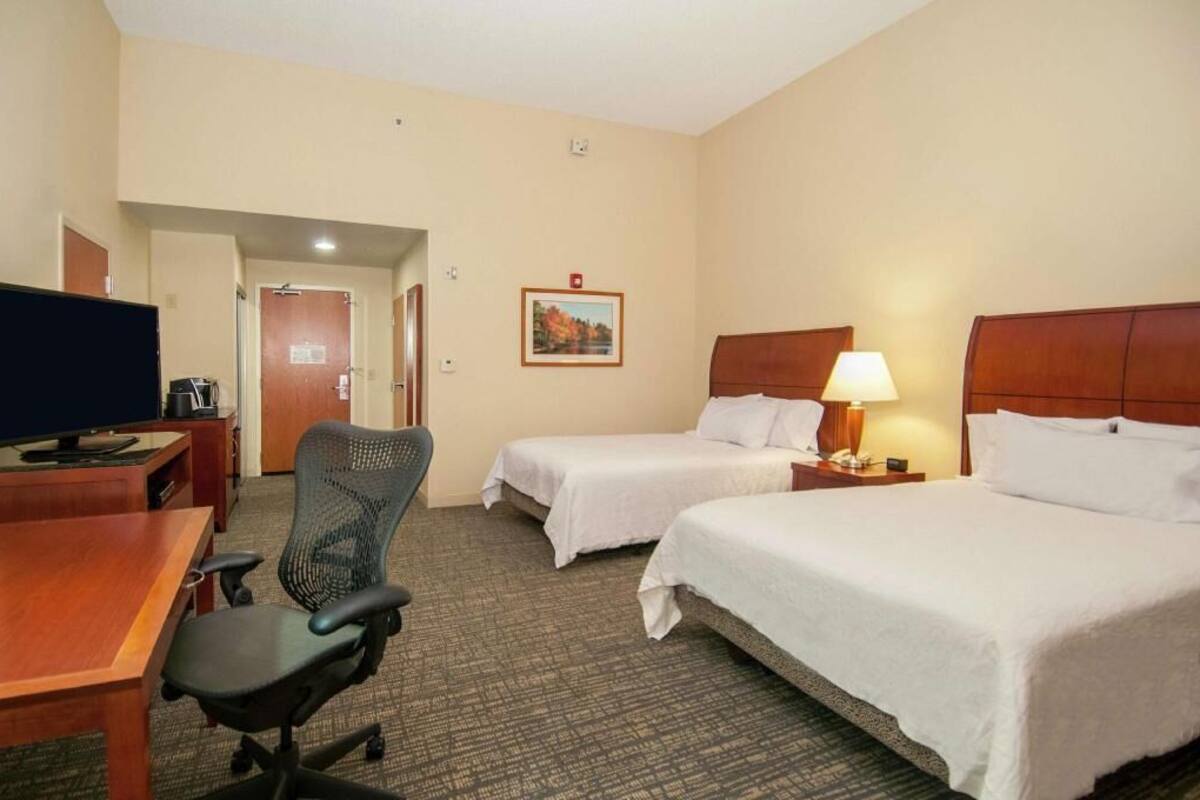 A hotel room with two beds, a desk, a chair, a television, and a framed picture on the wall.