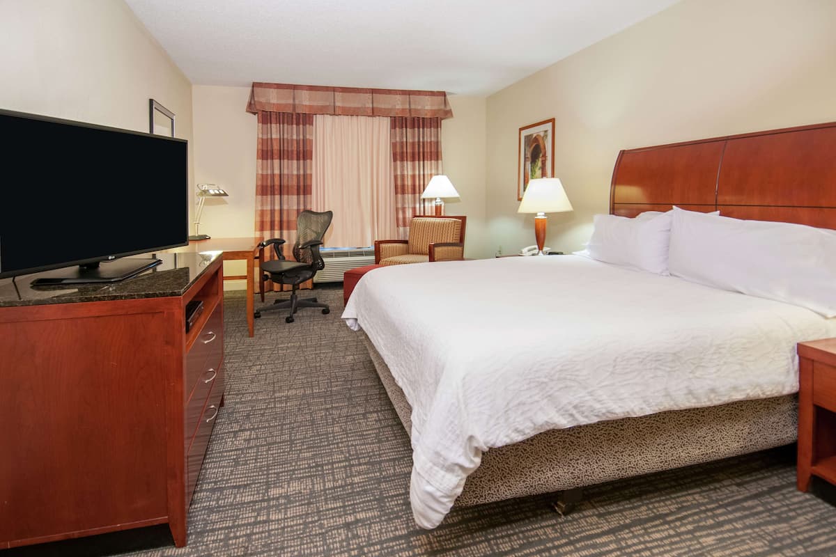 A hotel room with a large bed, a desk with a computer, a TV, and a chair.