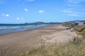 Une plage côtière avec un ciel dégagé, un rivage sablonneux et des bâtiments en arrière-plan.