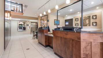 A hotel lobby with a reception desk, a mirror, and a view of the elevator area.