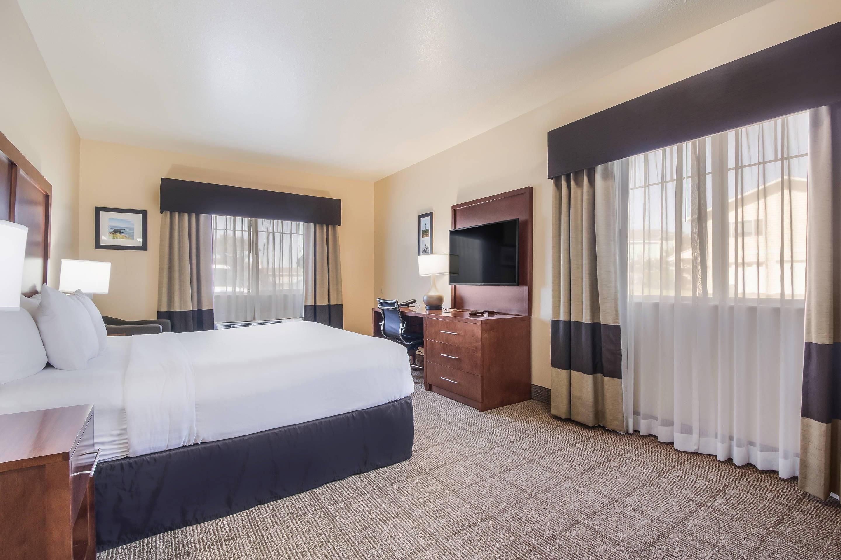 A hotel room with a large bed, a desk, a chair, a TV, and a wardrobe.