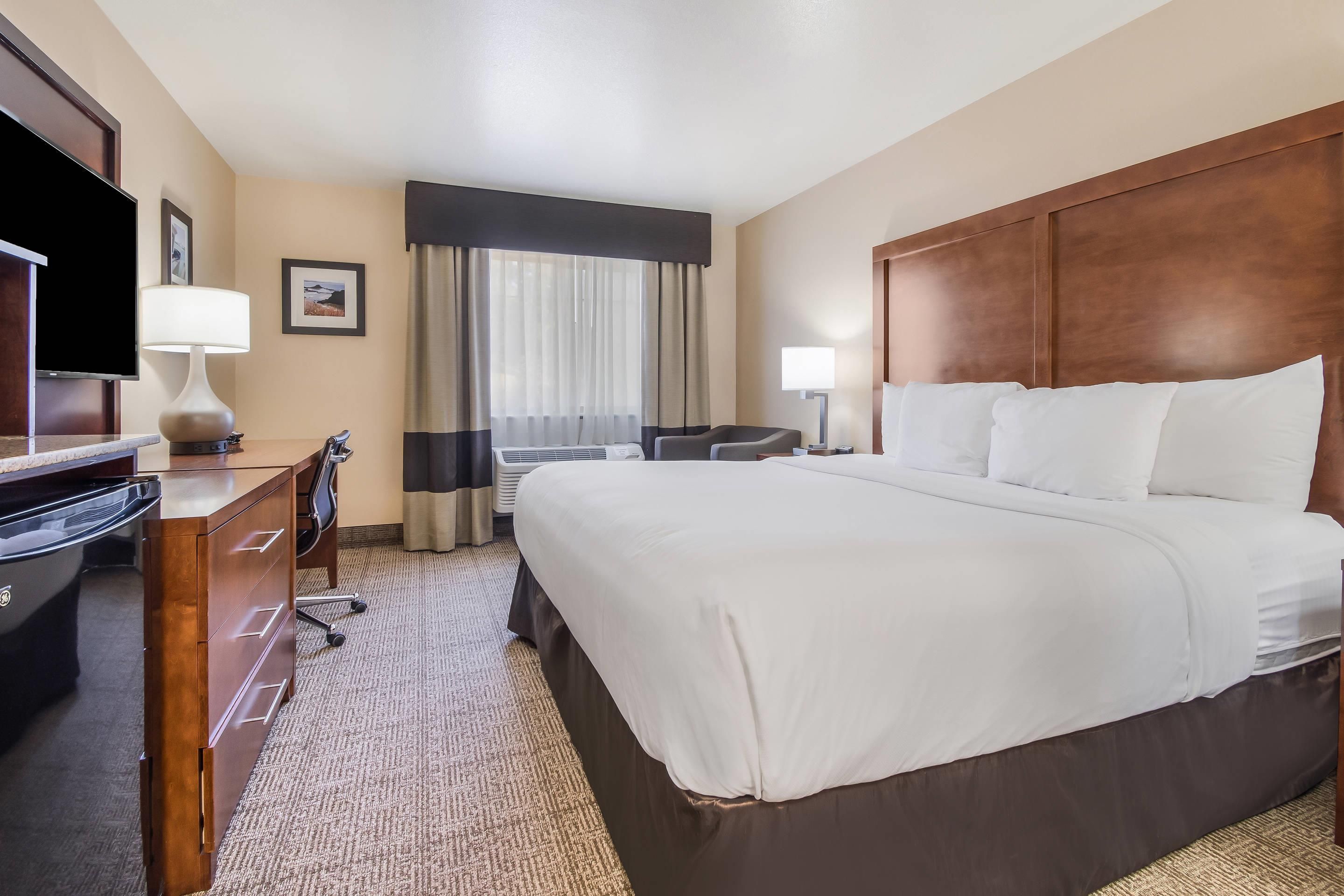 A hotel room with a large bed, a desk with a chair, a television, and a window with curtains.