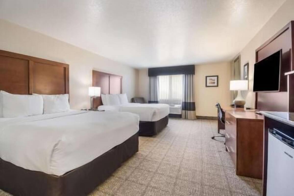 A hotel room with two beds, a desk, a TV, and a window with curtains.