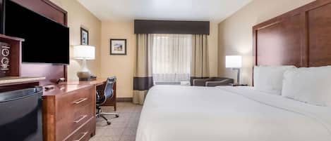 A hotel room with a large bed, a desk with a computer, a TV, and a chair.