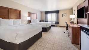 A hotel room with two beds, a desk, a television, and a window with curtains.