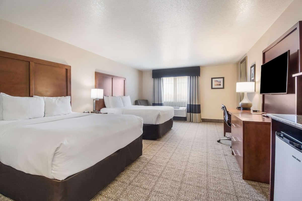 A hotel room with two beds, a desk, a television, and a window with curtains.