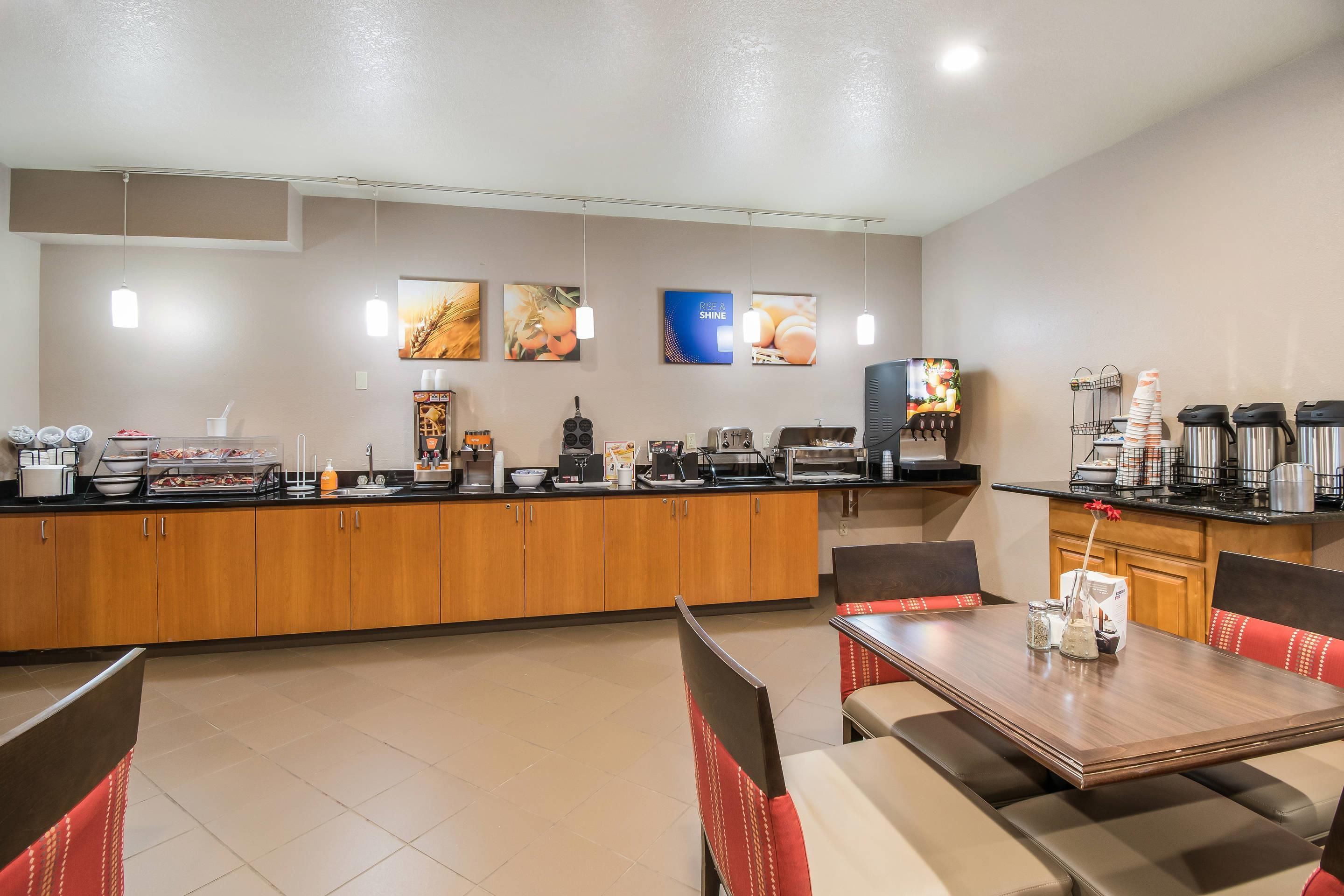 A hotel breakfast area with a counter, seating, and various food and beverage stations.
