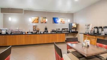 A hotel breakfast area with a counter, seating, and various food and beverage stations.