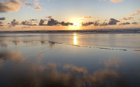 A beach with a calm sea and a sunset in the background.