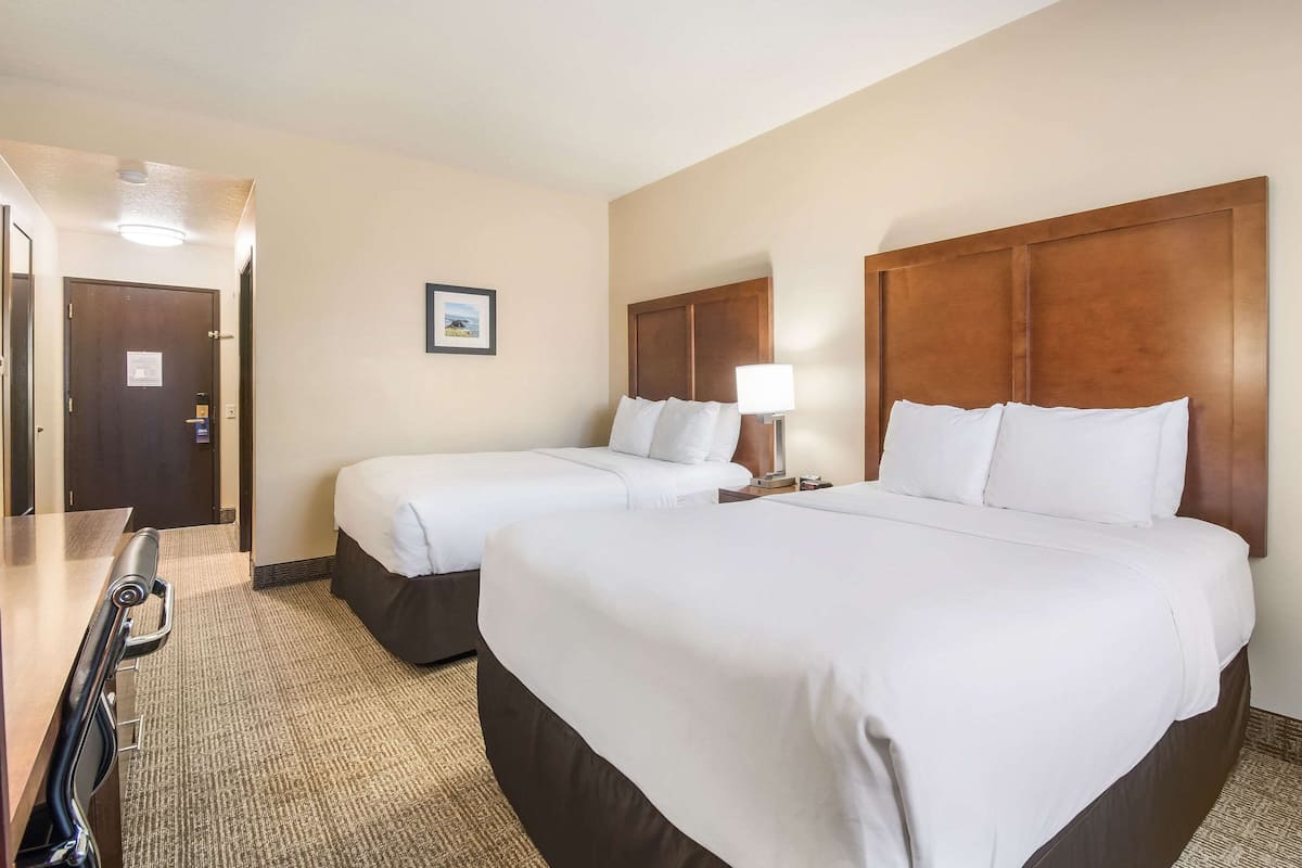 A hotel room with two beds, a desk with a chair, a lamp, and a framed picture on the wall.
