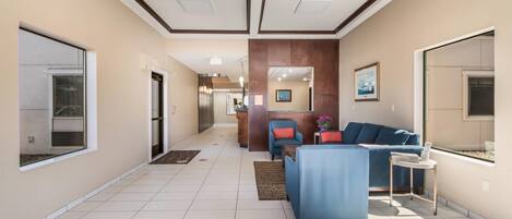 A modern hotel lobby with a reception desk, seating area, and a view of the hallway.