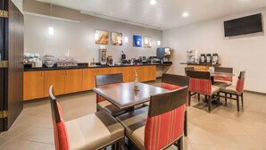 A hotel dining area with a counter, chairs, tables, and a TV mounted on the wall.