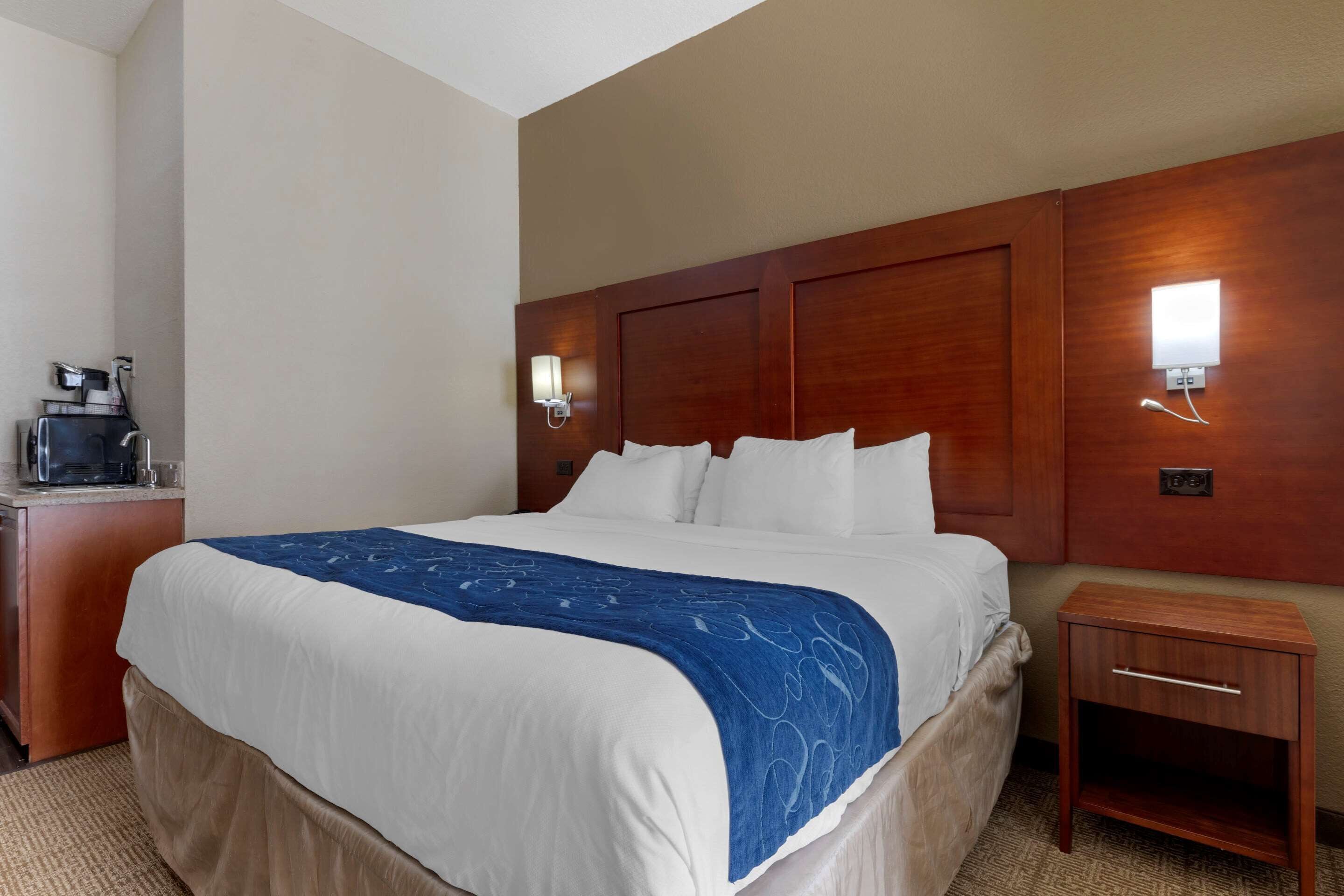 Une chambre d’hôtel avec un grand lit, une tête de lit en bois, une table de chevet et une lampe fixée au mur.
