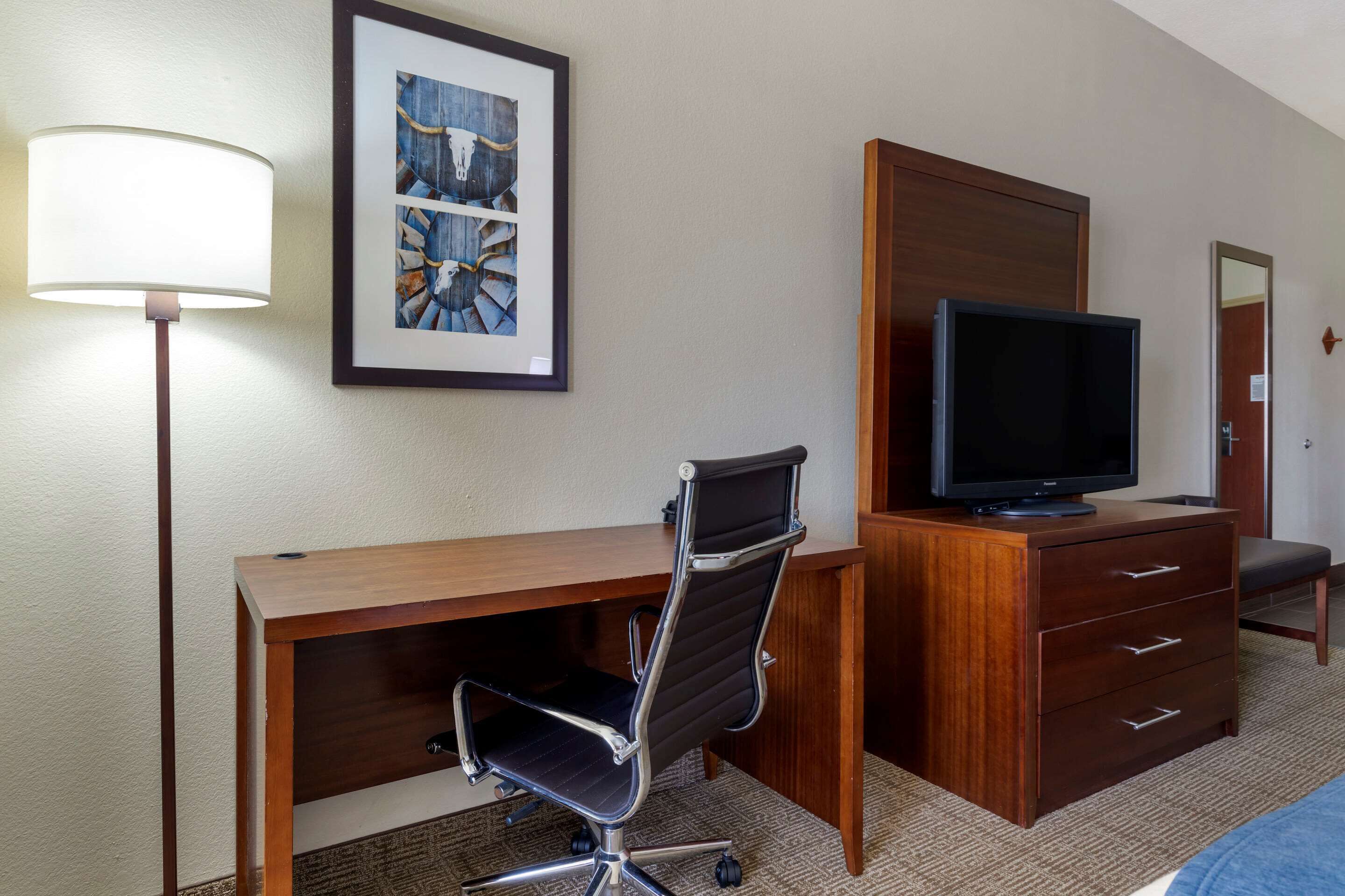 Habitación de hotel con escritorio de madera, una silla de oficina negra, televisor sobre un aparador de madera y un cuadro en la pared.