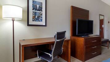 Habitación de hotel con escritorio de madera, una silla de oficina negra, televisor sobre un aparador de madera y un cuadro en la pared.