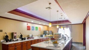 Una cocina de hotel con una isla central, armarios de madera y una barra para desayunar.