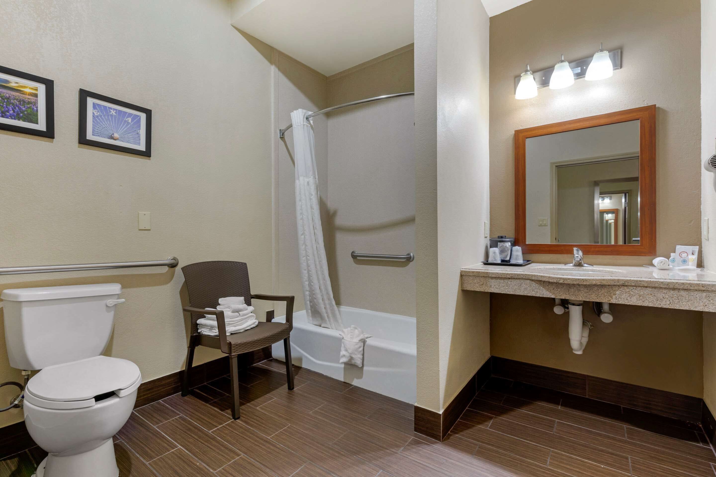 A bathroom with a toilet, shower, chair, and sink with a mirror.