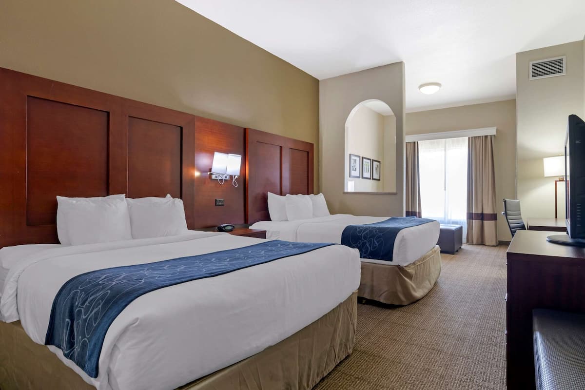A hotel room with two beds, a desk, a television, and a window with curtains.