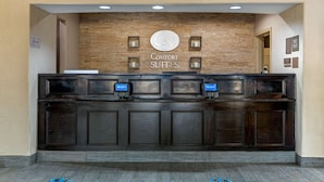 Un mostrador de recepción con un letrero que dice "Comfort Suites". Hay dos quioscos digitales y un mostrador de atención al cliente.