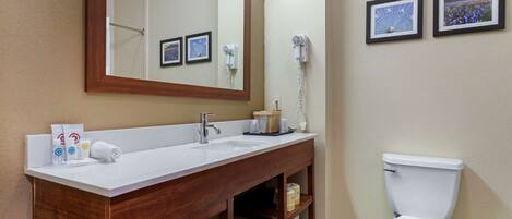 A bathroom with a wooden vanity, a white sink, a mirror, a white toilet, and two framed pictures on the wall.