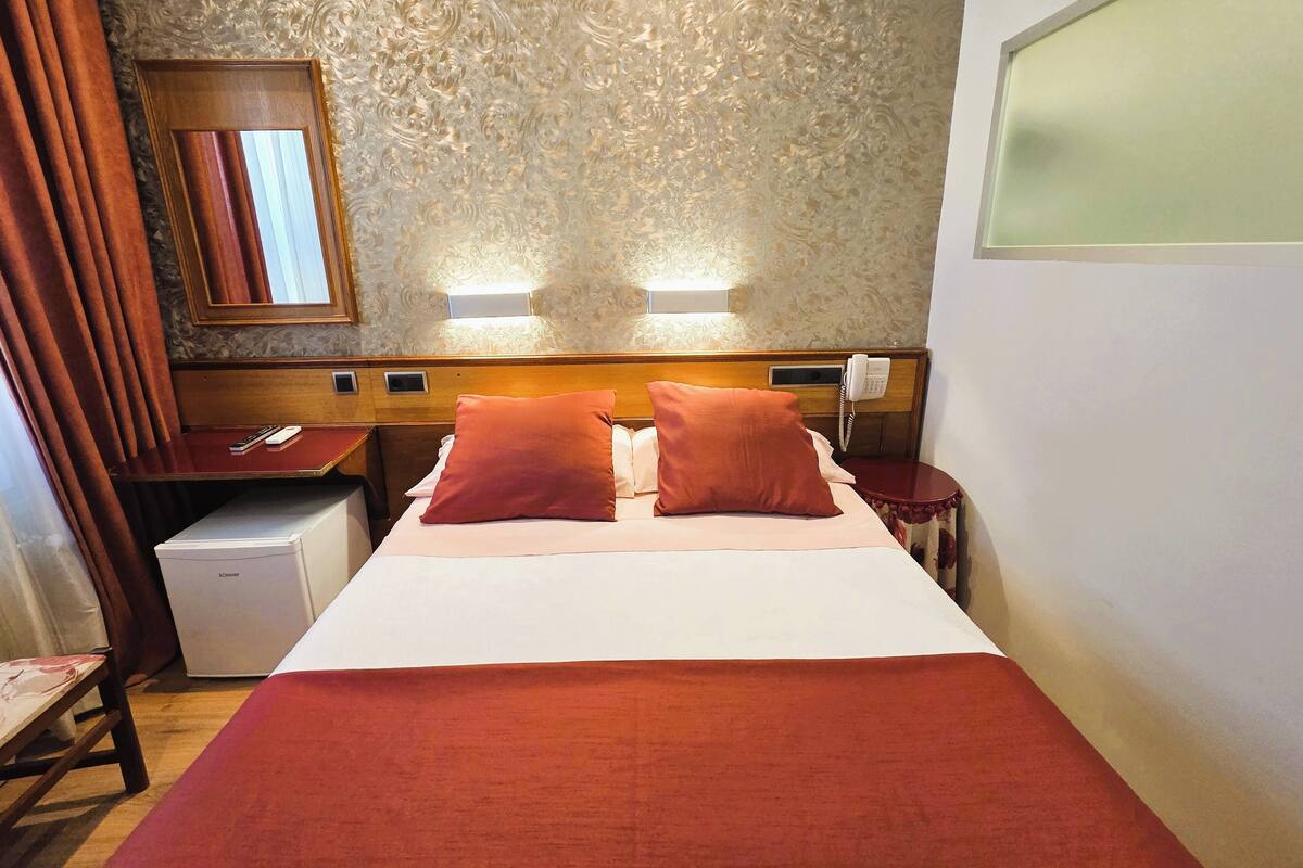 Een hotelkamer met een bed, twee nachtkastjes, een bureau, een spiegel en een aan de muur bevestigd telefoontoestel.