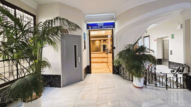 A hotel lobby with a marble floor, potted plants, and a sign for 'HISPANO ARGENTINO'.