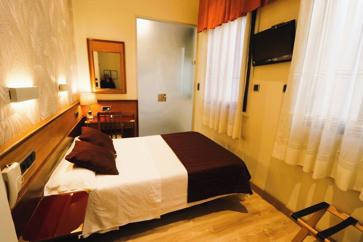 Hotelkamer met een bed, bureau, stoel, televisie aan de muur en een deur naar een andere kamer.