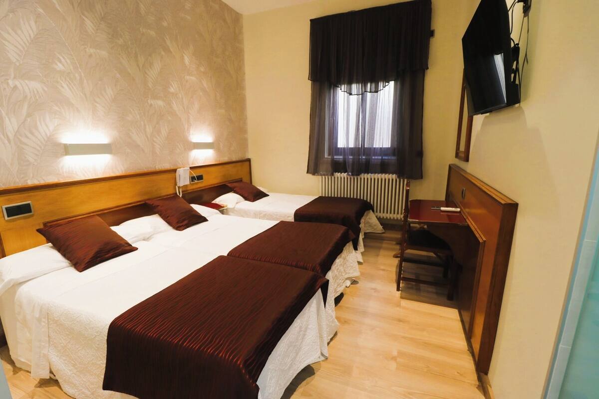 Hotelkamer met twee bedden, een bureau, een stoel, een televisie en een raam met gordijnen.