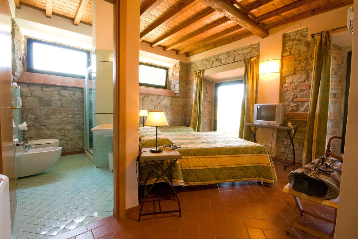 Ein Schlafzimmer mit Bett, Fernseher, Lampe und einem Badezimmer mit Waschbecken und Toilette.