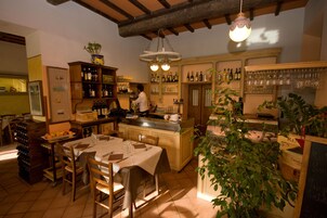 Un acogedor interior de restaurante con una zona de bar, muebles de madera y una variedad de botellas y vasos en estantes.