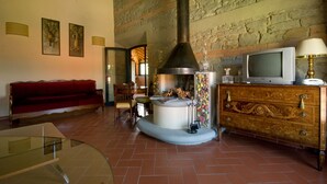 A cozy living room with a fireplace, a red sofa, a wooden cabinet, and a television. - Hotel Gli Orzali (Firenzuola)