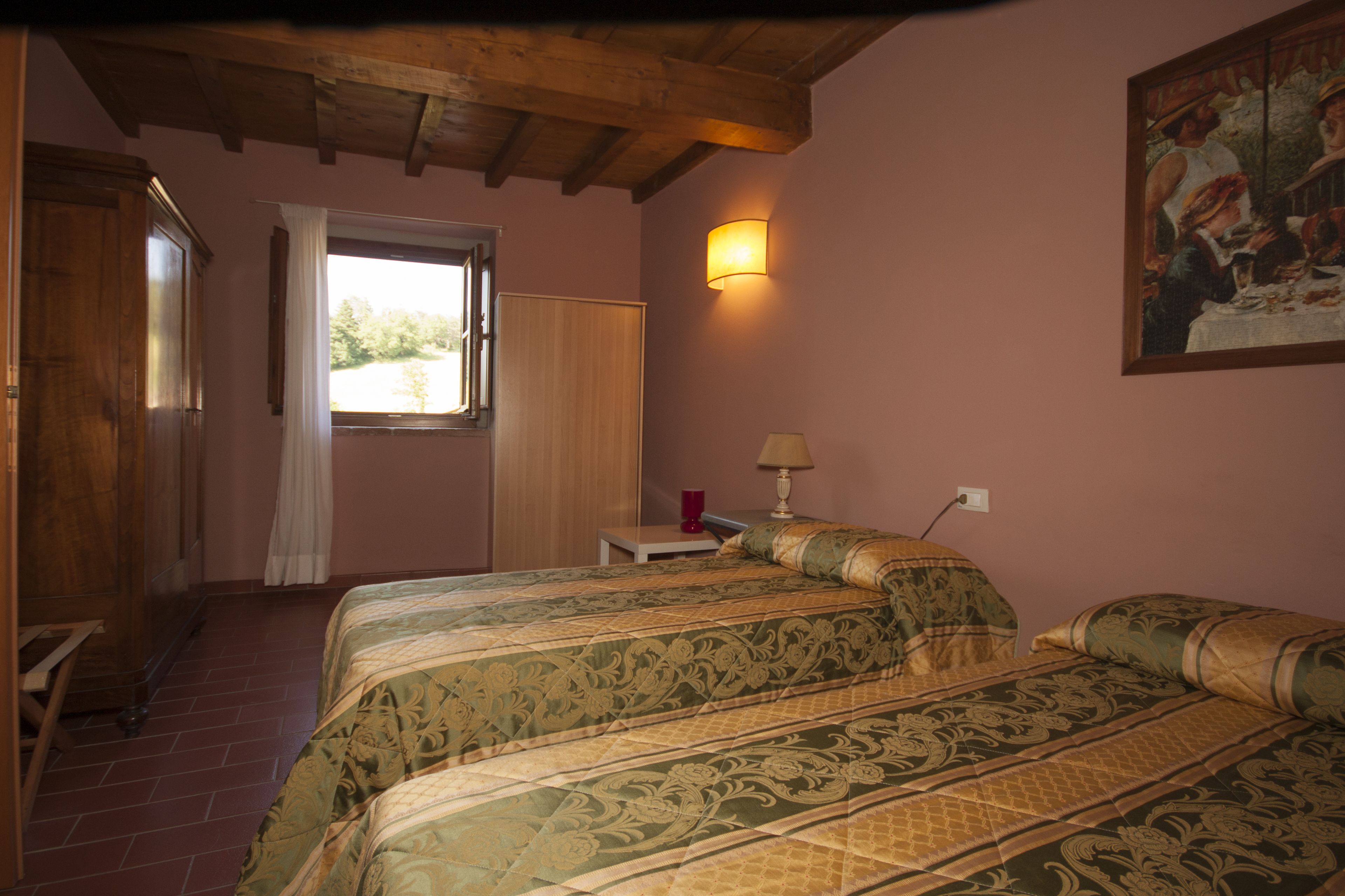 A room with two beds, a window with curtains, a lamp on a bedside table, and a painting on the wall.