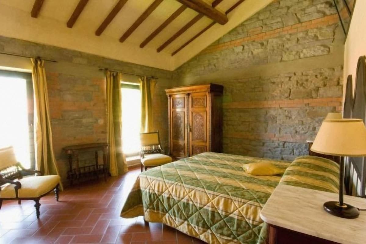 Un dormitorio con cama, mesita de noche, lámpara, sillón y chimenea.