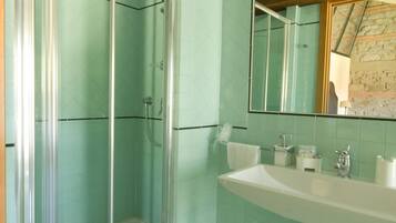 A bathroom with a glass shower enclosure, a sink with a mirror, and tiled walls.
